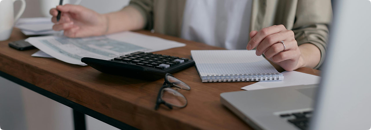 Personne travaillant dans un cabinet d'expertise comptable, avec calculatrice, documents financiers, stylo et ordinateur